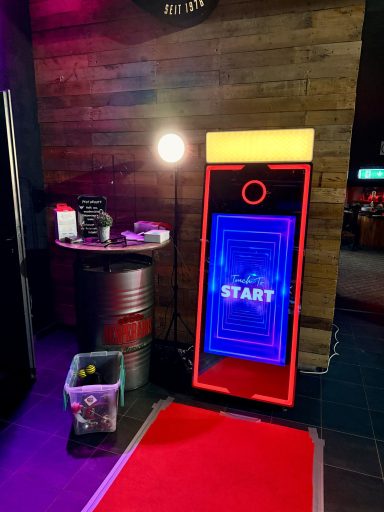 Ein leuchtendes, rotes Gerät mit der Aufschrift "START" vor einem Tisch und einer Mülltonne.